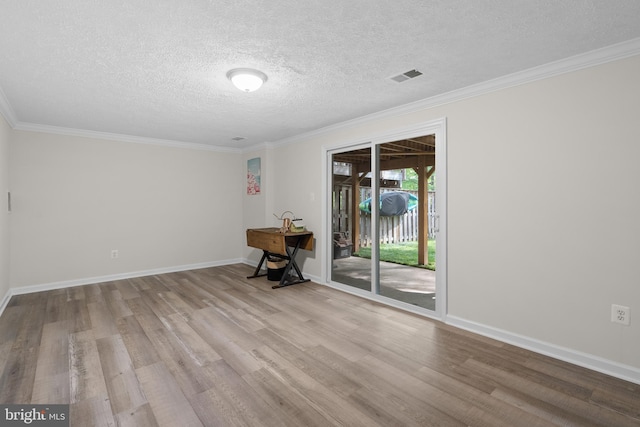 empty room with visible vents, wood finished floors, a textured ceiling, and ornamental molding