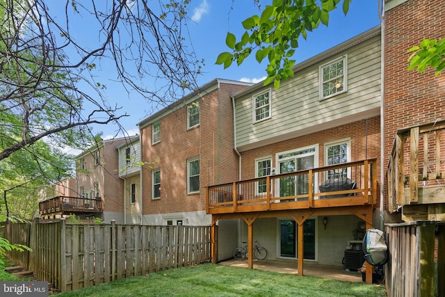 back of property with brick siding, fence private yard, a wooden deck, a patio area, and a lawn