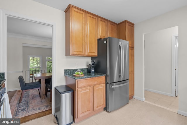 kitchen featuring dark stone counters, freestanding refrigerator, brown cabinetry, and baseboards