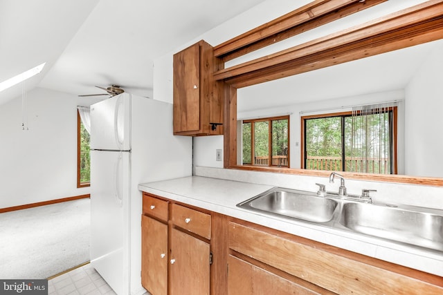 kitchen featuring vaulted ceiling with skylight, a sink, light countertops, freestanding refrigerator, and brown cabinetry
