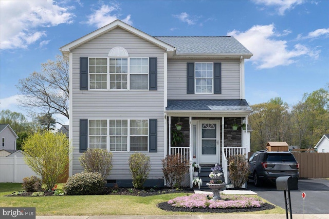 traditional home with fence, covered porch, and roof with shingles