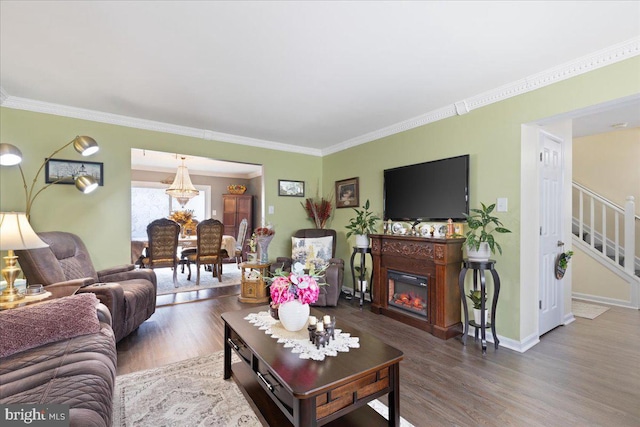 living room featuring wood finished floors, ornamental molding, a glass covered fireplace, and stairs