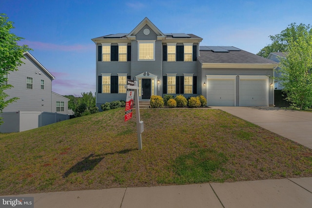 colonial home featuring a yard, driveway, fence, solar panels, and a garage