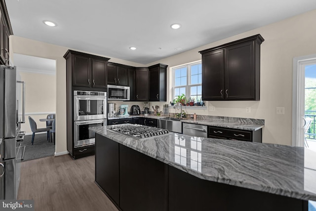 kitchen featuring wood finished floors, a sink, plenty of natural light, appliances with stainless steel finishes, and light stone counters