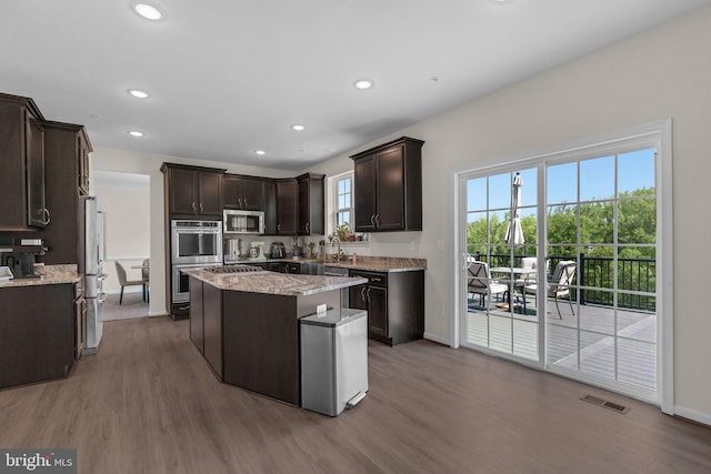 kitchen featuring a center island, wood finished floors, stainless steel appliances, dark brown cabinetry, and visible vents