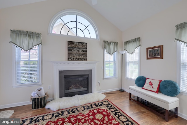living room with baseboards, a glass covered fireplace, wood finished floors, and vaulted ceiling