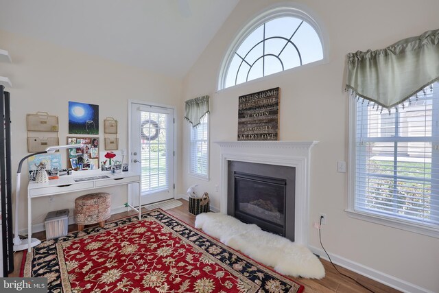 living room with a glass covered fireplace, wood finished floors, high vaulted ceiling, and baseboards