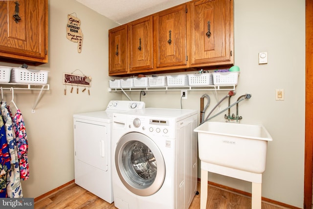 clothes washing area featuring washing machine and clothes dryer, baseboards, light wood-type flooring, and cabinet space