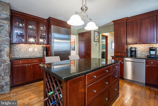 kitchen with backsplash, a textured ceiling, appliances with stainless steel finishes, and light wood-style floors