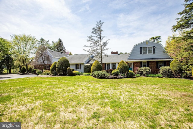 view of front of home with brick siding, a front lawn, and a gambrel roof