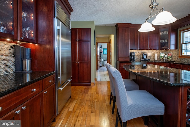 kitchen with tasteful backsplash, light wood finished floors, built in fridge, and dark brown cabinets