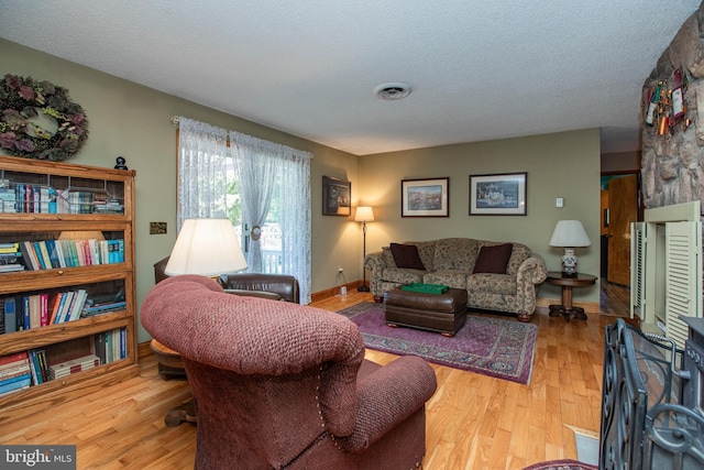 living room with visible vents, baseboards, a textured ceiling, and wood finished floors