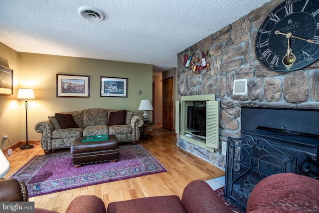 living area with a textured ceiling, visible vents, a stone fireplace, and wood finished floors