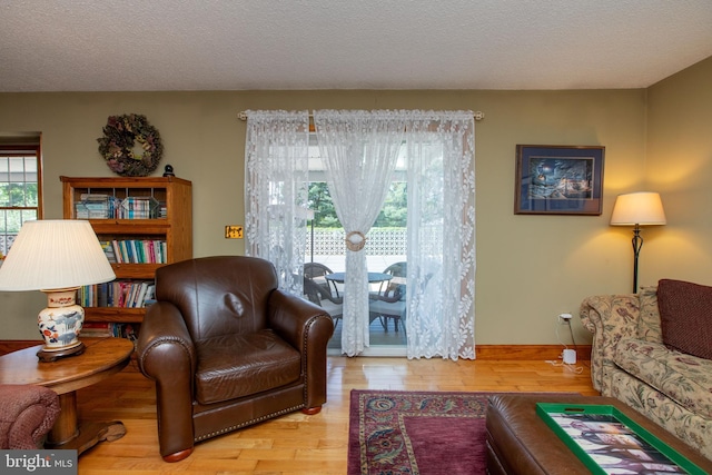living area with baseboards, a textured ceiling, and wood finished floors