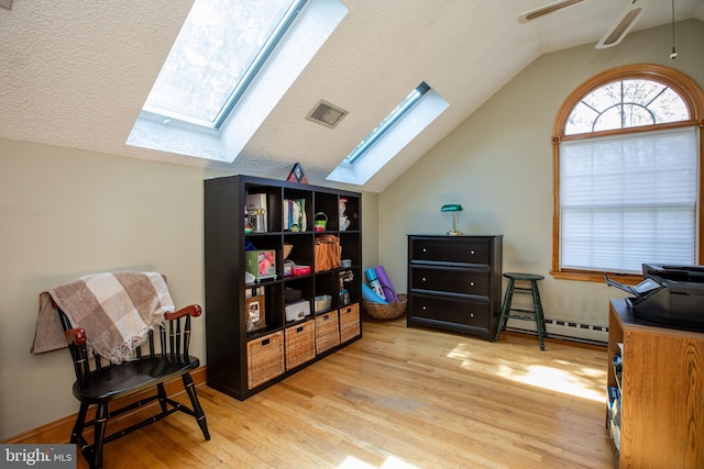 interior space featuring ceiling fan, visible vents, wood finished floors, a baseboard radiator, and lofted ceiling with skylight