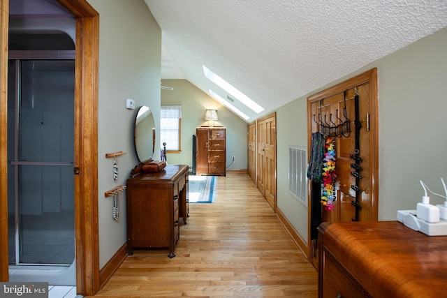 hall with vaulted ceiling with skylight, a textured ceiling, baseboards, light wood-type flooring, and visible vents
