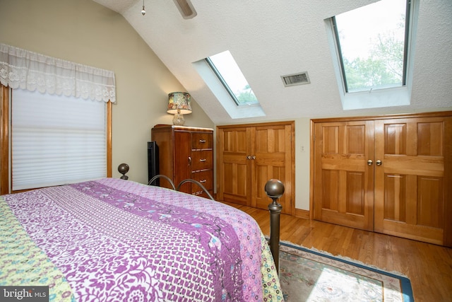 bedroom with ceiling fan, visible vents, wood finished floors, and vaulted ceiling with skylight