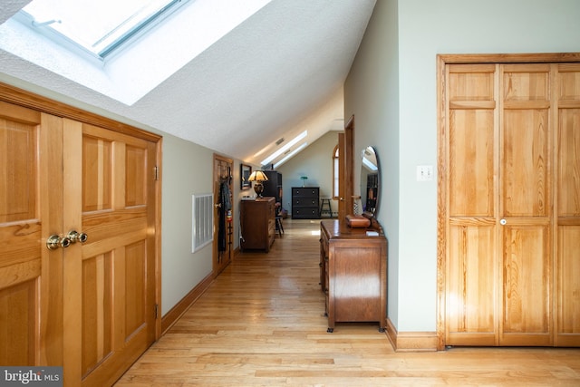 additional living space featuring vaulted ceiling with skylight, baseboards, light wood finished floors, and visible vents
