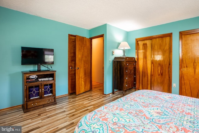 bedroom featuring two closets, baseboards, and wood finished floors