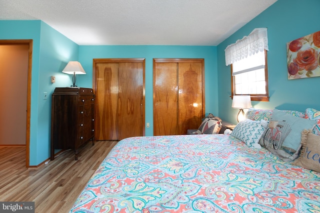 bedroom with baseboards, a textured ceiling, multiple closets, and wood finished floors