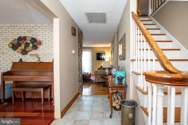 hallway with a textured ceiling, visible vents, tile patterned floors, baseboards, and stairs