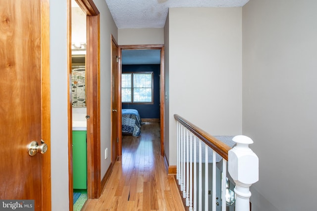 hallway with a textured ceiling, baseboards, an upstairs landing, and hardwood / wood-style flooring