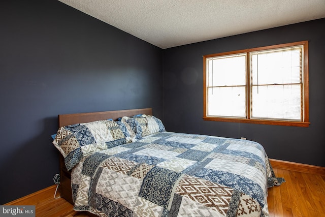 bedroom with baseboards, a textured ceiling, and wood finished floors