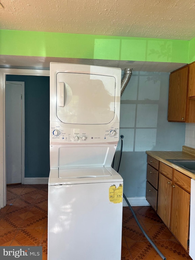 7601 Somerset Ln, Manassas, VA 20111 - washroom featuring stacked washer and clothes dryer, a textured ceiling, dark tile patterned flooring, and baseboards