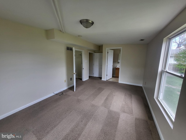 unfurnished bedroom featuring carpet, multiple closets, visible vents, baseboards, and ensuite bathroom