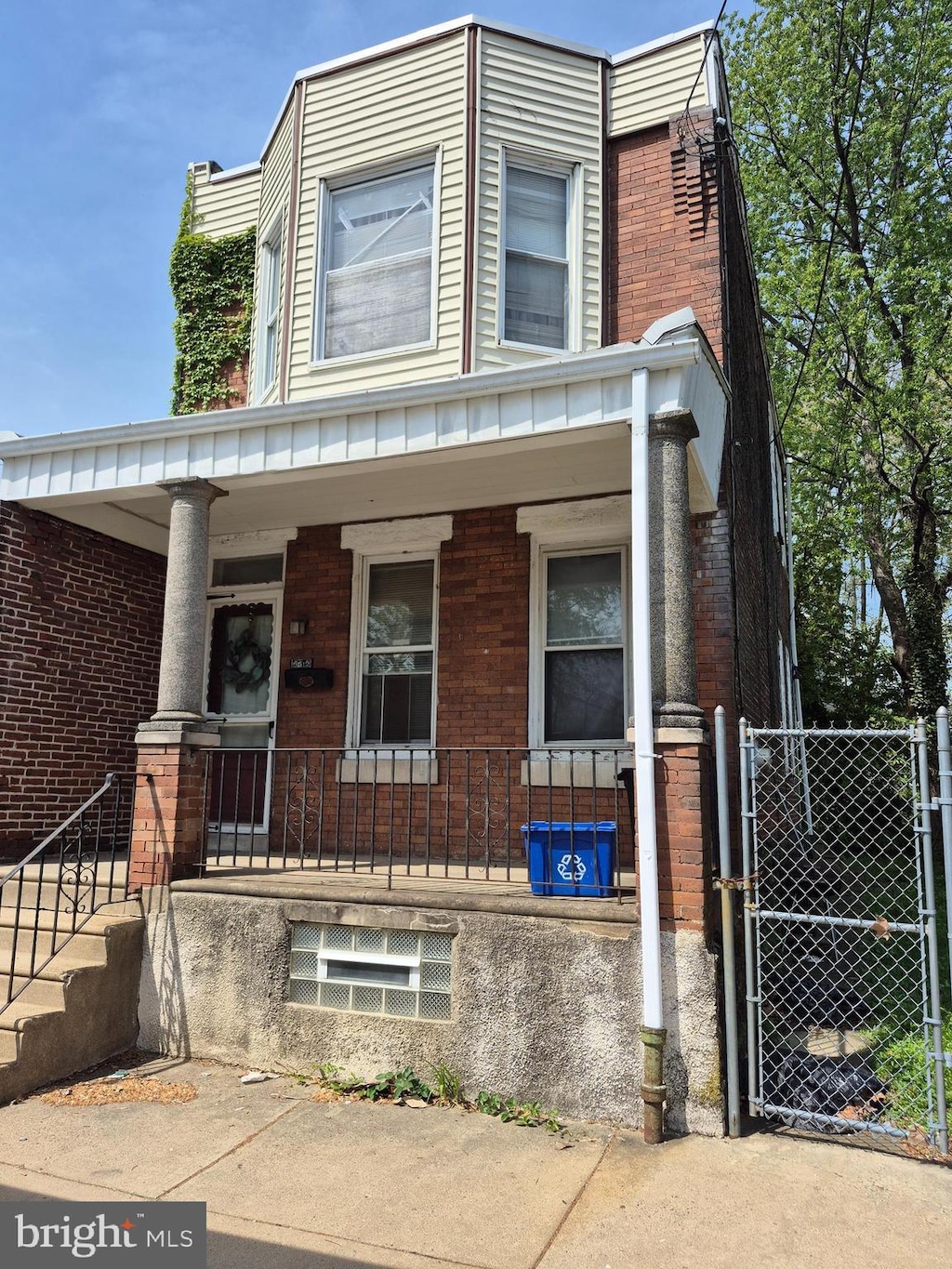 view of front of house with a porch, brick siding, fence, and a gate