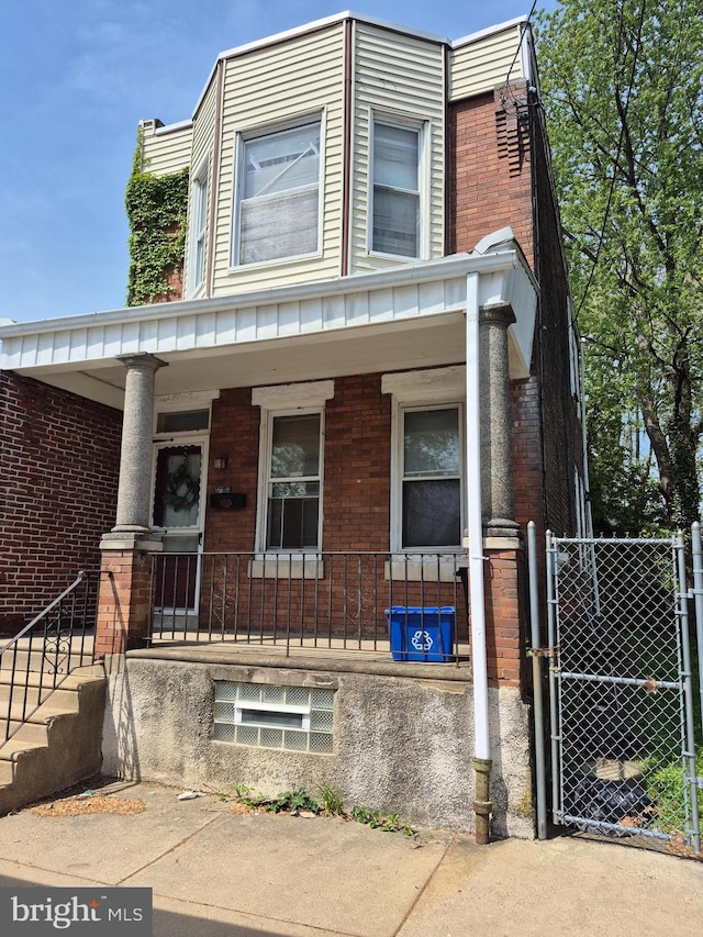 view of front of house with a porch, brick siding, fence, and a gate