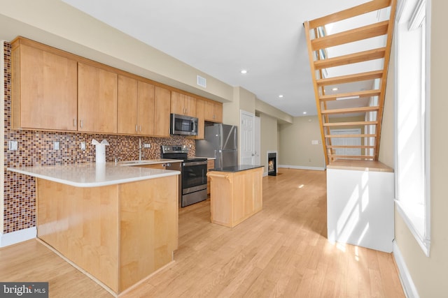 kitchen featuring light wood finished floors, decorative backsplash, a kitchen bar, baseboards, and appliances with stainless steel finishes