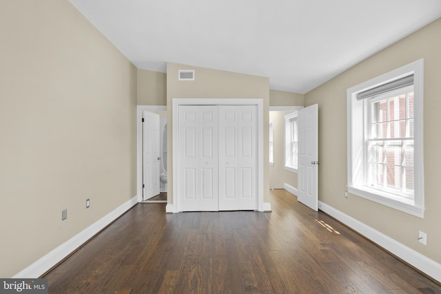 unfurnished bedroom featuring a closet, visible vents, multiple windows, and dark wood-type flooring