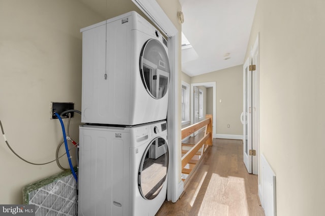 laundry area featuring baseboards, stacked washer / dryer, wood finished floors, and laundry area