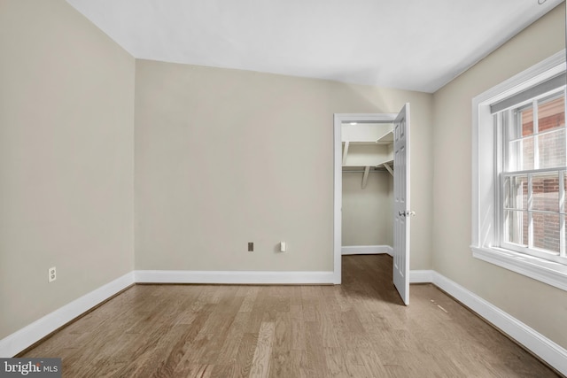 unfurnished bedroom featuring multiple windows, a spacious closet, light wood finished floors, and baseboards