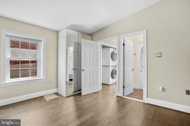 unfurnished bedroom with wood finished floors, ensuite bathroom, stacked washer / dryer, and baseboards