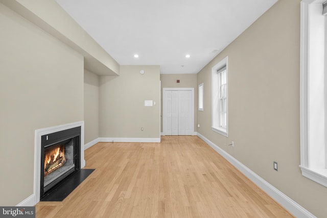 unfurnished living room with light wood finished floors, recessed lighting, a fireplace with flush hearth, and baseboards