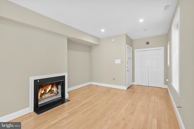 unfurnished living room with recessed lighting, light wood-style floors, baseboards, visible vents, and a fireplace with flush hearth