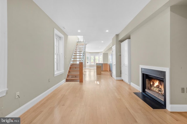 corridor with baseboards, light wood-type flooring, and stairway