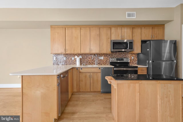 kitchen with appliances with stainless steel finishes, light wood finished floors, a sink, visible vents, and a peninsula