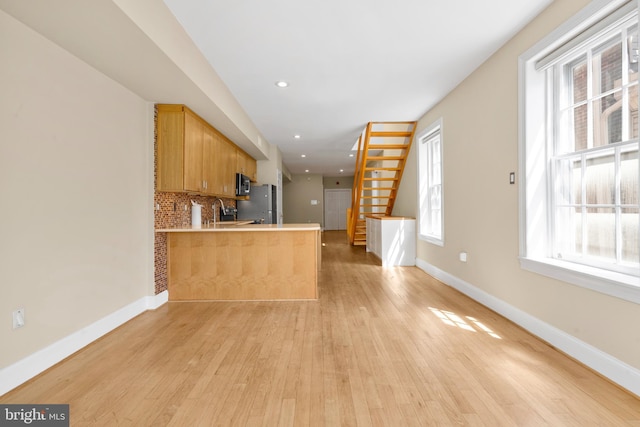 kitchen featuring decorative backsplash, stainless steel appliances, light wood finished floors, baseboards, and a peninsula