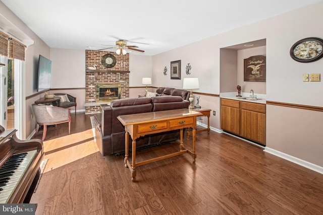 living room with baseboards, ceiling fan, a brick fireplace, and dark wood finished floors