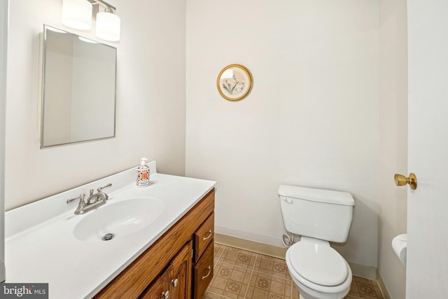 half bath featuring vanity, baseboards, tile patterned floors, and toilet
