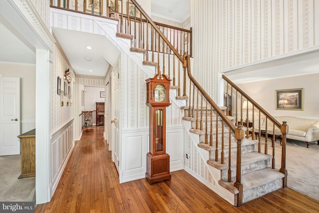 staircase featuring crown molding, a wainscoted wall, wallpapered walls, and hardwood / wood-style floors
