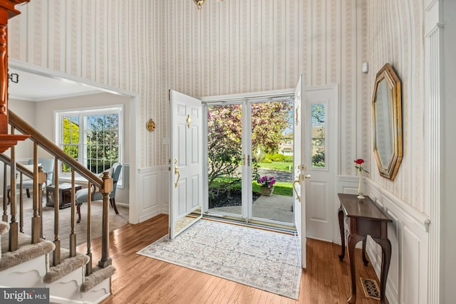 entrance foyer with stairs, wallpapered walls, wainscoting, and wood finished floors