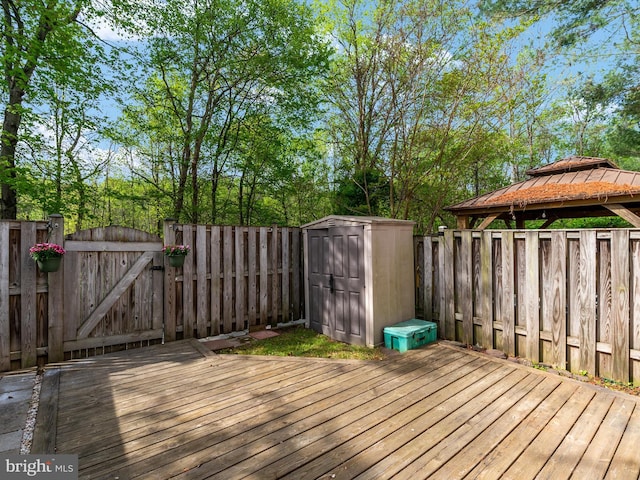 wooden terrace with an outdoor structure, a storage unit, a fenced backyard, and a gate