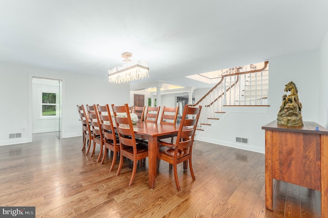dining space featuring wood finished floors, a chandelier, stairs, and baseboards