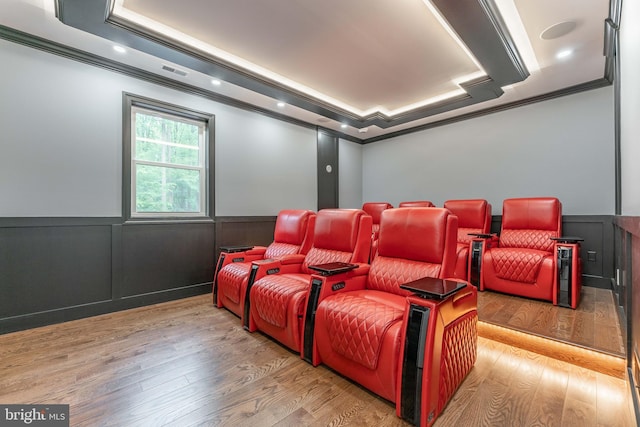 cinema room with crown molding, a wainscoted wall, wood finished floors, a decorative wall, and a raised ceiling