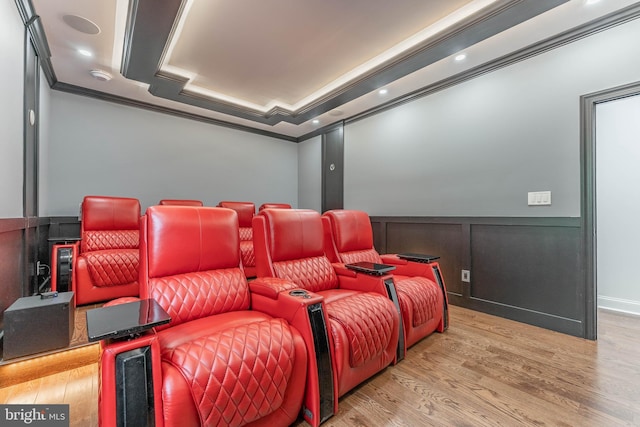 home theater room featuring crown molding, wood finished floors, a wainscoted wall, and a decorative wall