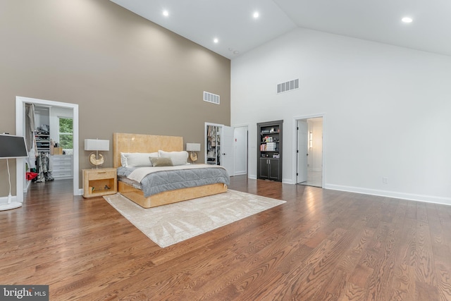 bedroom with a walk in closet, high vaulted ceiling, wood finished floors, baseboards, and recessed lighting